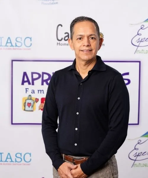Abel Covarrubias posing in front of an Aprendamos Family of Services backdrop