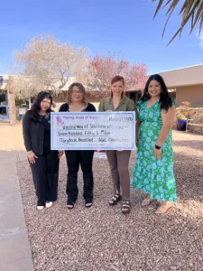 Four women stand outside holding a large ceremonial check for $750 presented to United Way of Southwest New Mexico for the Storybook Breakfast.